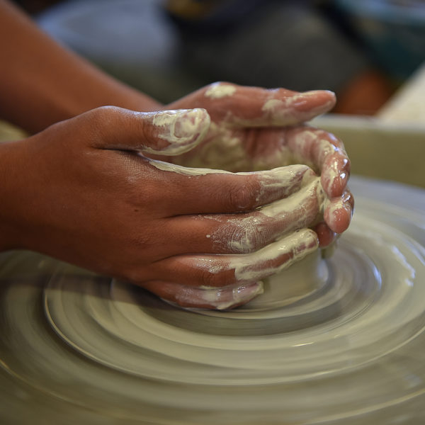 two hands working clay on a throwing wheel